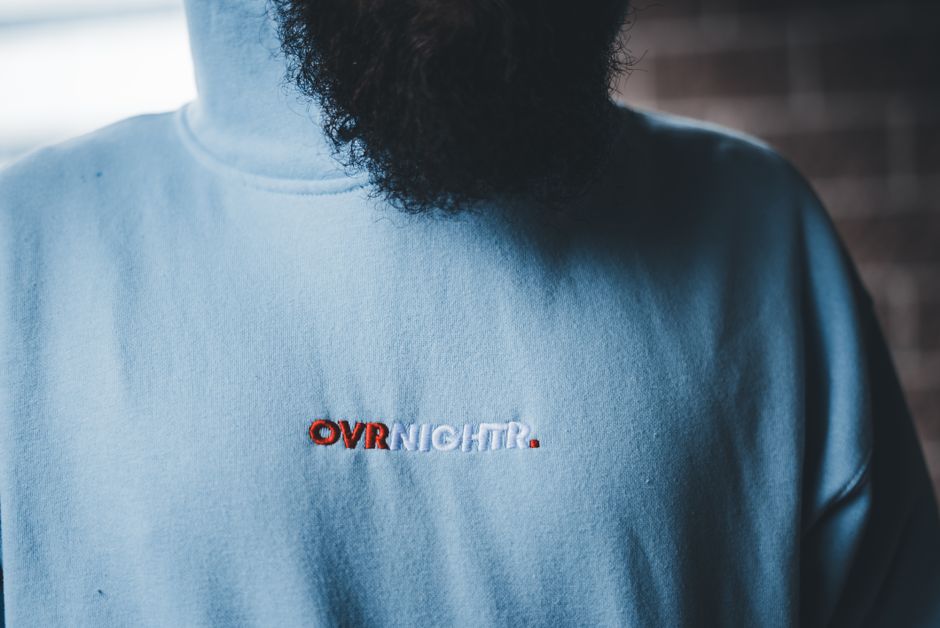 broderie de logo — Gros plan détaillé sur un hoodie bleu avec texte brodé et vue partielle d'une barbe.