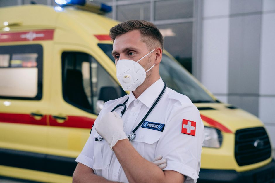 communication visuelle — Paramédical portant un masque et un stéthoscope, se tenant confiant devant une ambulance.